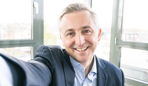 Trusted Shops CEO Jean-Marc Noel smiles at the camera and takes a selfie in his office.
